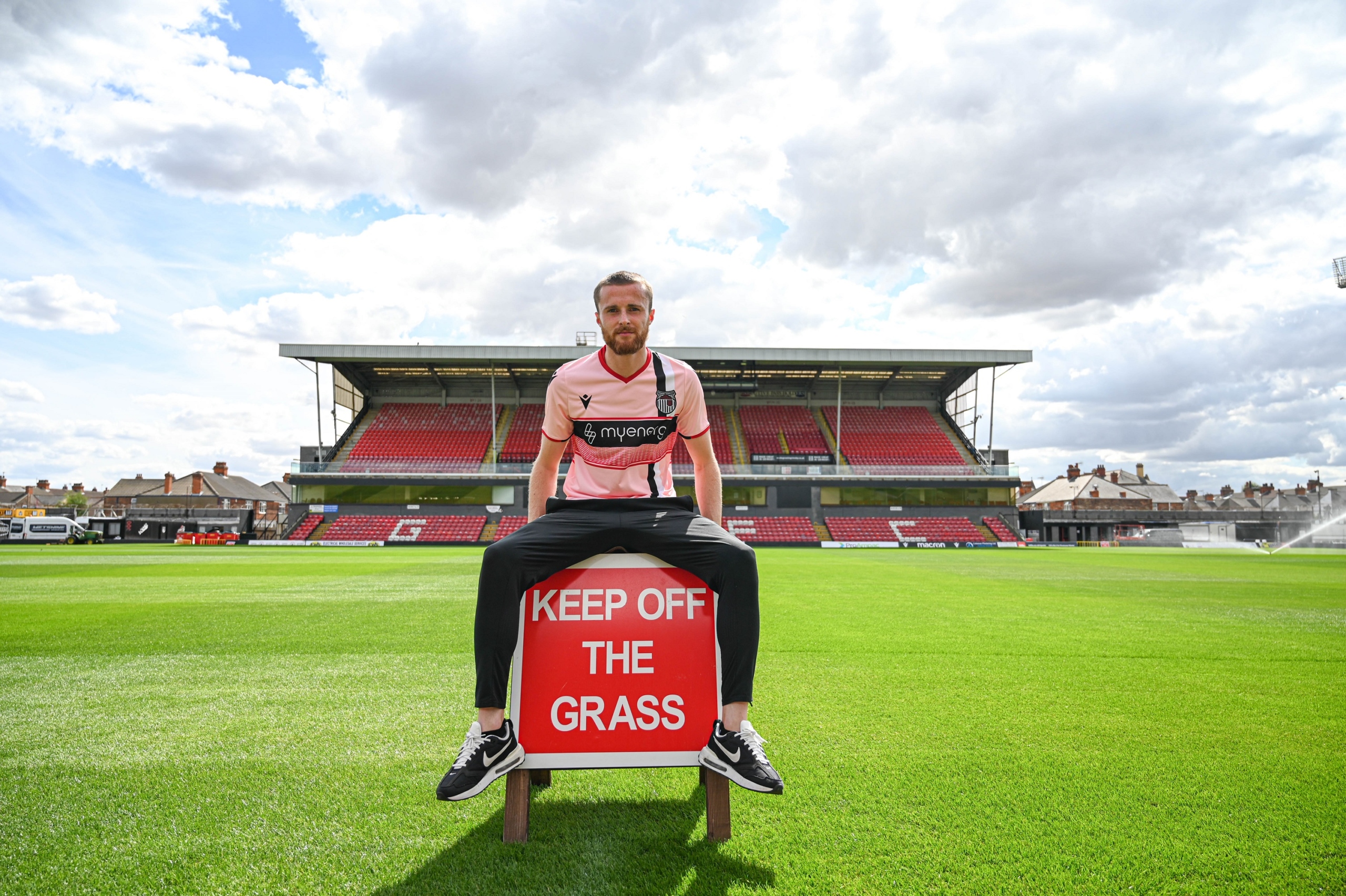 Niall Maher sitting on a keep off the grass sign